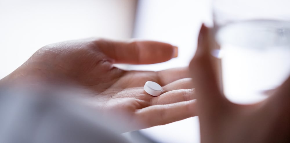 A woman holding her medicine on the palm of her hand with a glass of water in the other hand.